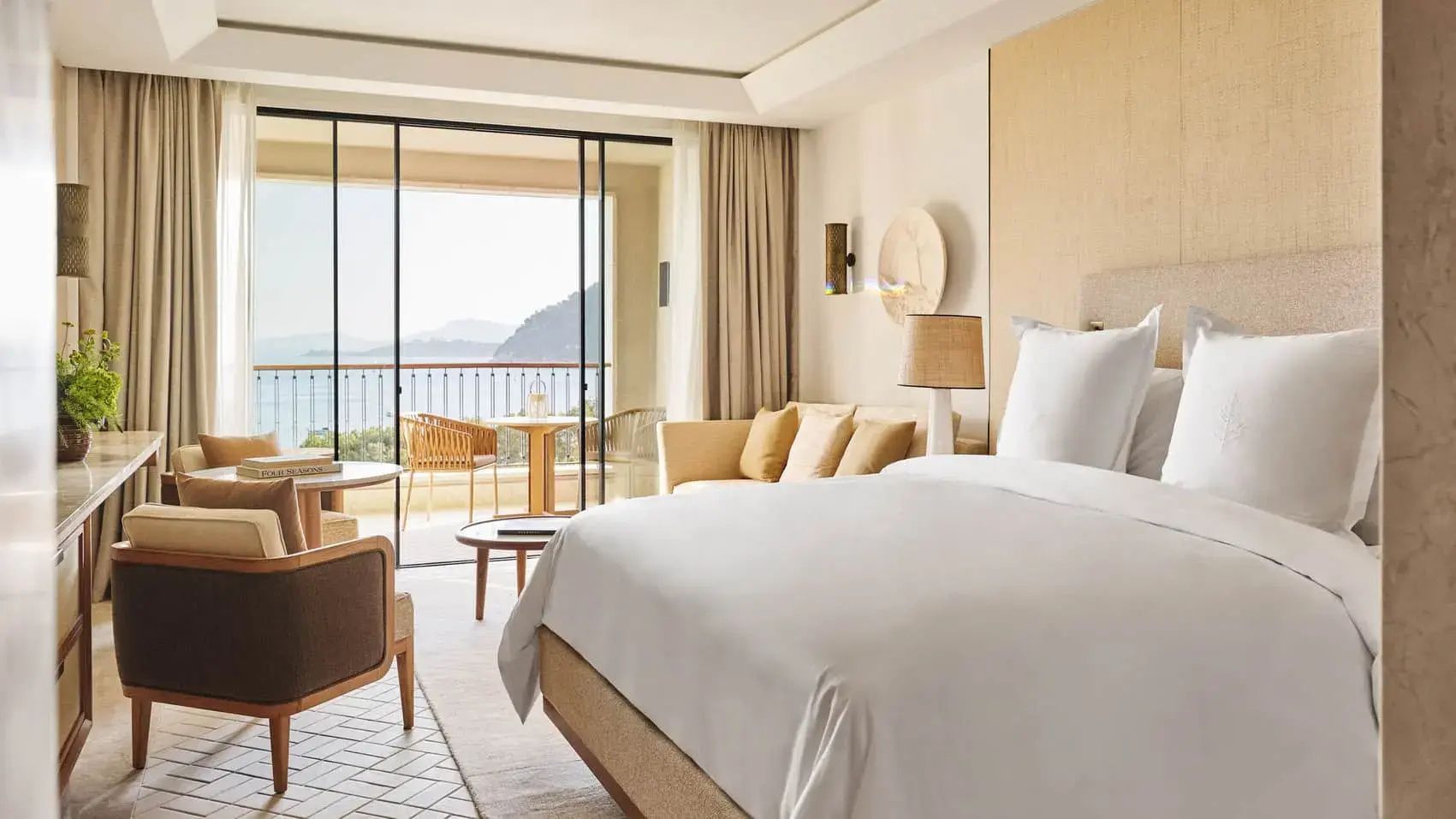 Helles Hotelzimmer mit großem Doppelbett, Sofa und Balkon mit Meerblick.
