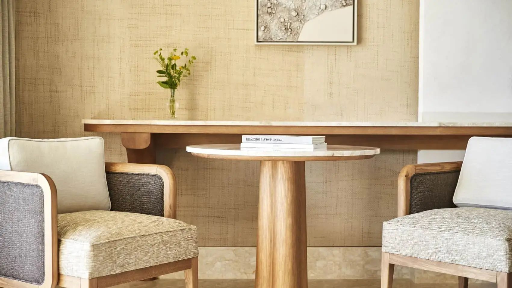 Sitzbereich mit rundem Holztisch, Stühlen und kleiner Blumenvase an der Wand.