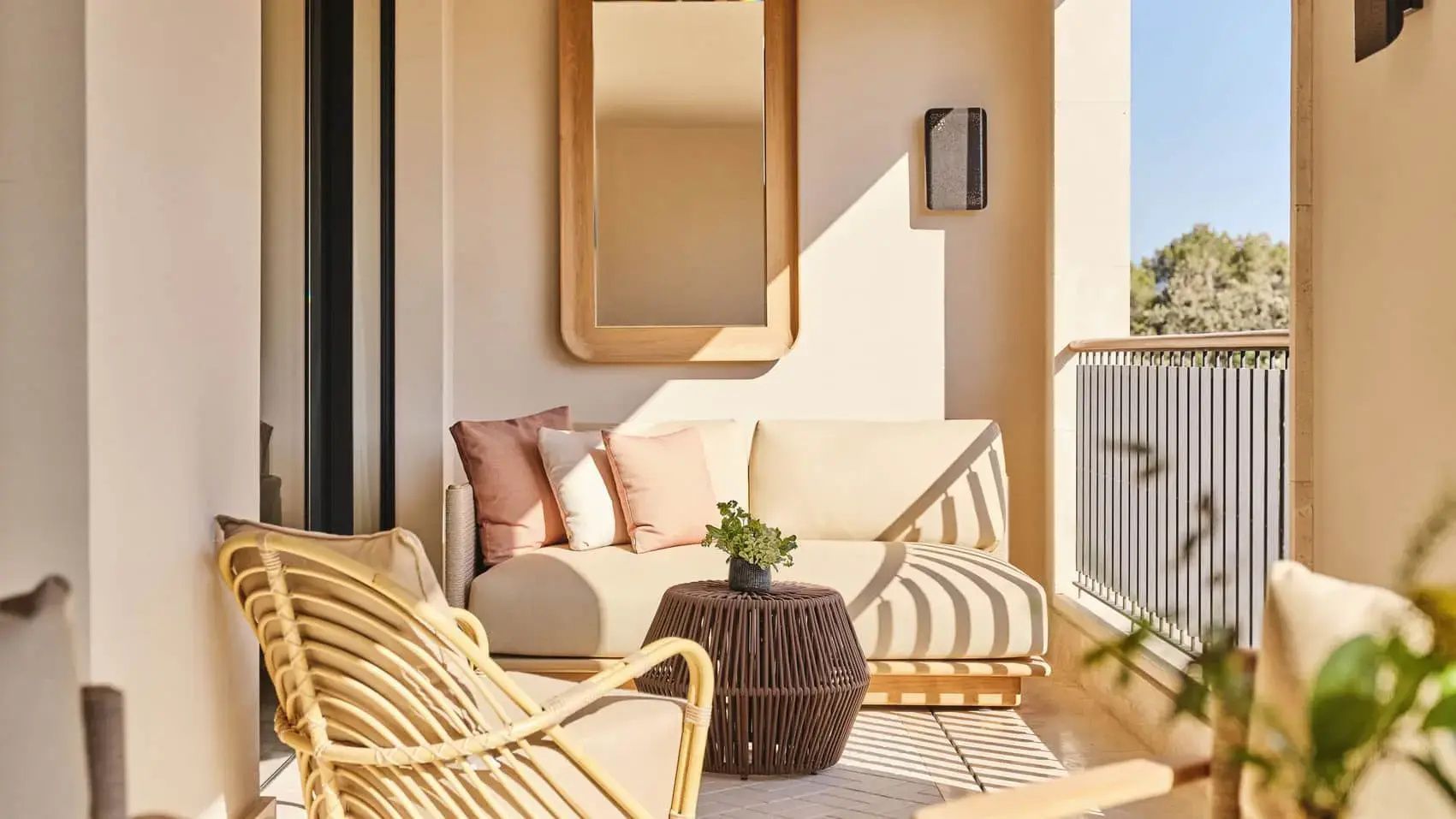 Überdachter Balkon mit bequemem Sofa, Kissen, Tisch und Holzspiegel an der Wand.