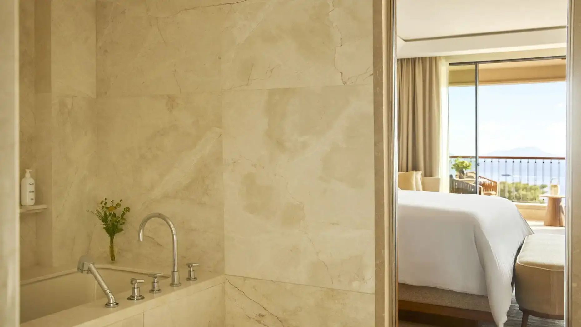 Marmoriertes Badezimmer mit Wanne und Blick in das angrenzende Schlafzimmer.