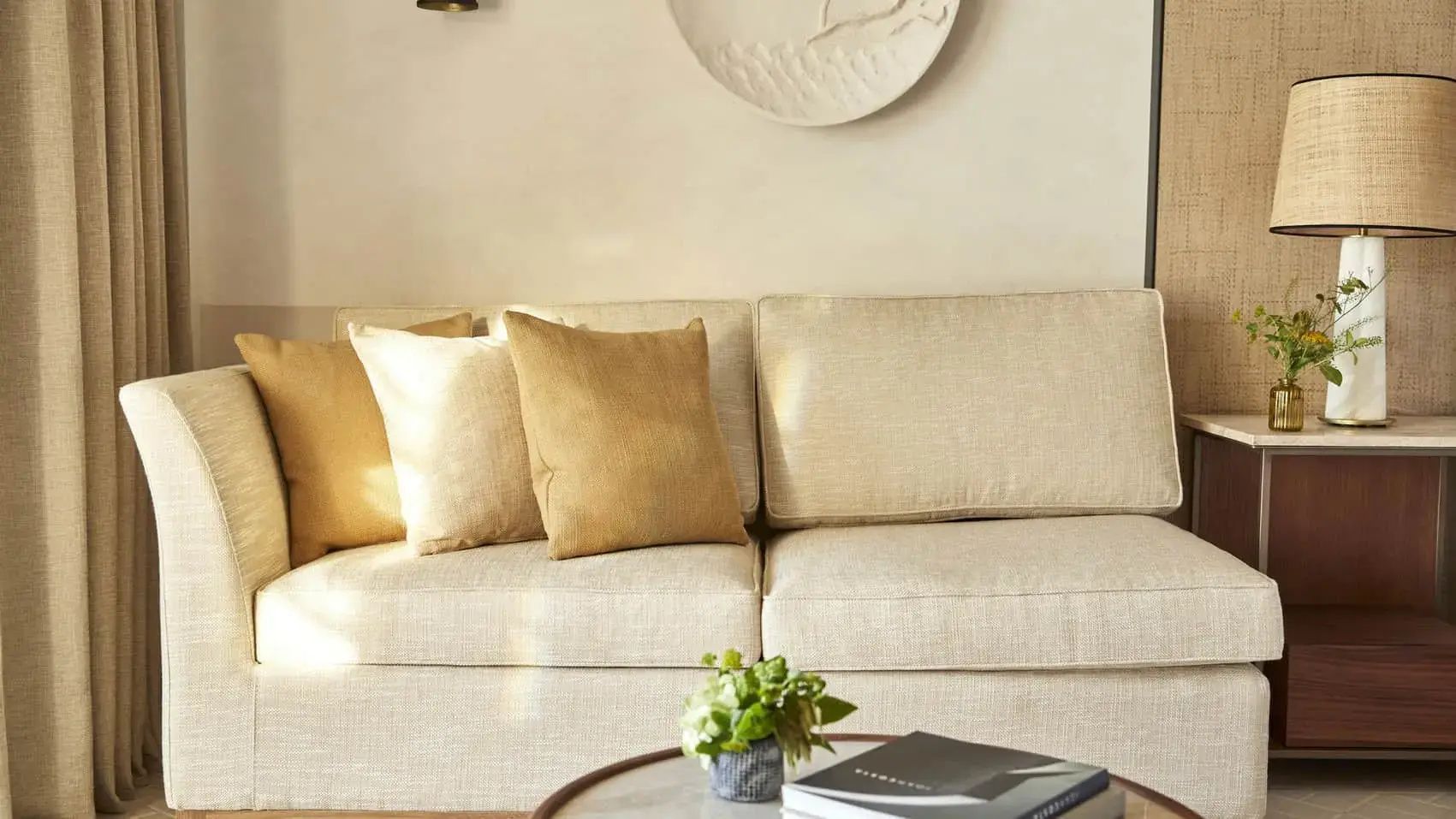 Helles beigefarbenes Sofa mit Kissen und ein Beistelltisch mit Pflanze im Wohnbereich.