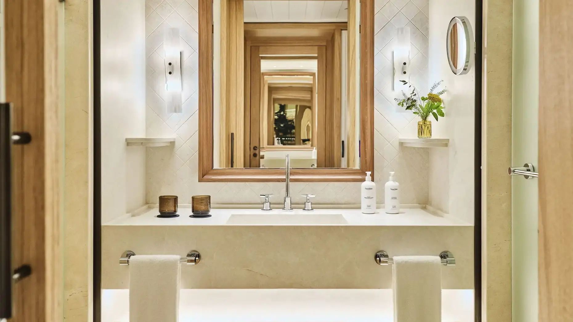 Waschtisch im Badezimmer mit großem Spiegel, Wandleuchten und Seifenspendern.