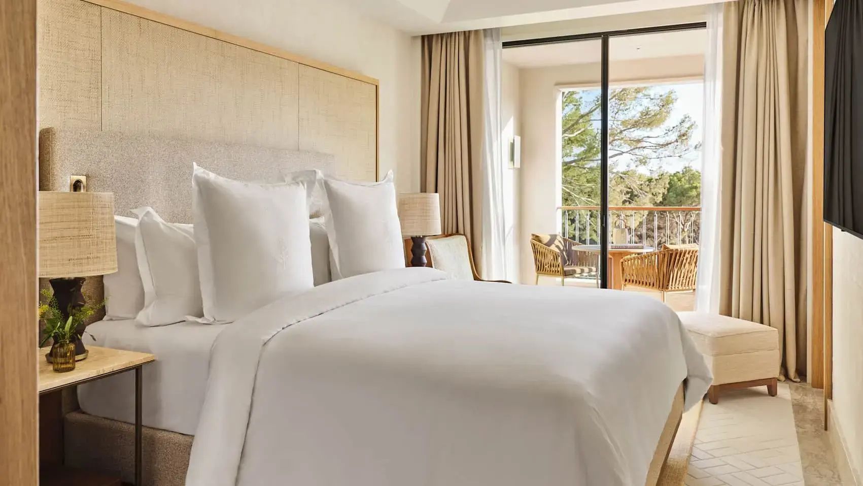 Hell eingerichtetes Hotelzimmer mit Doppelbett und Blick auf den Balkon.