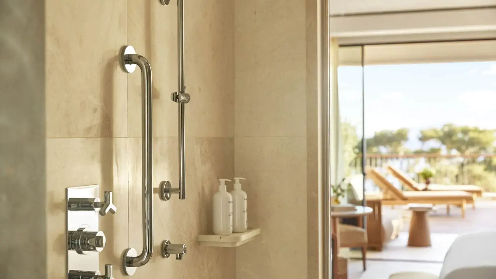 Badezimmer mit Dusche, Metallhaltegriff und Pflegeflaschen auf einer Wandablage.