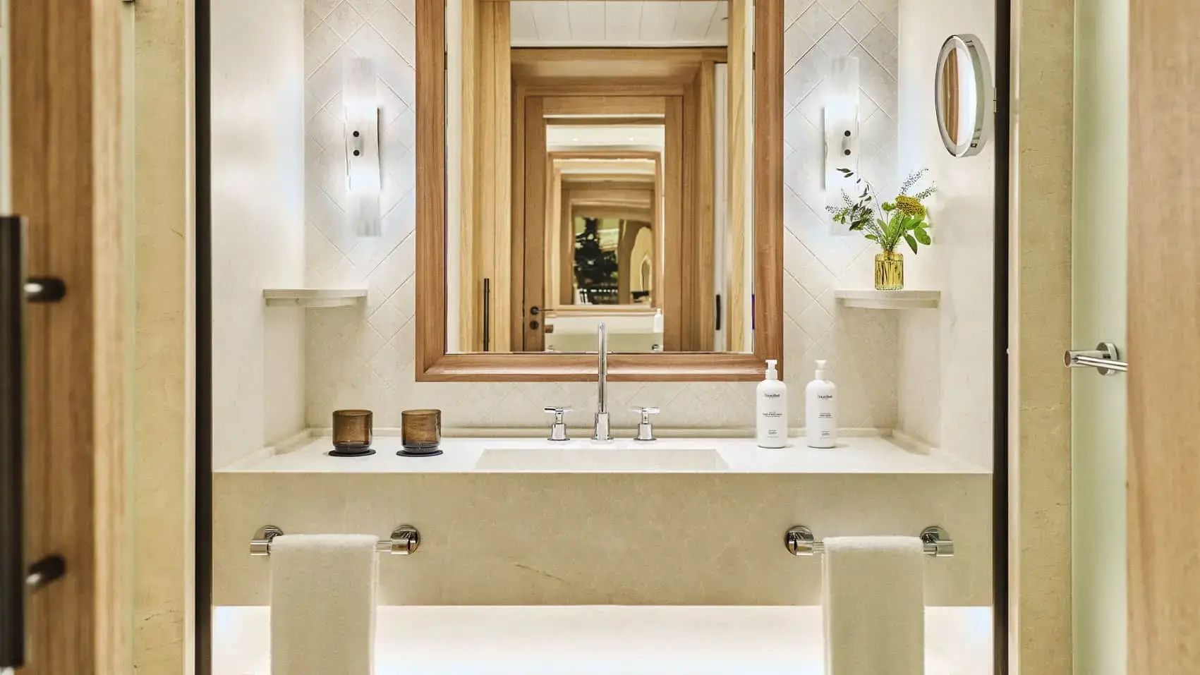 Badezimmer mit hellem Einzelwaschtisch, Handtüchern und Wandleuchten.
