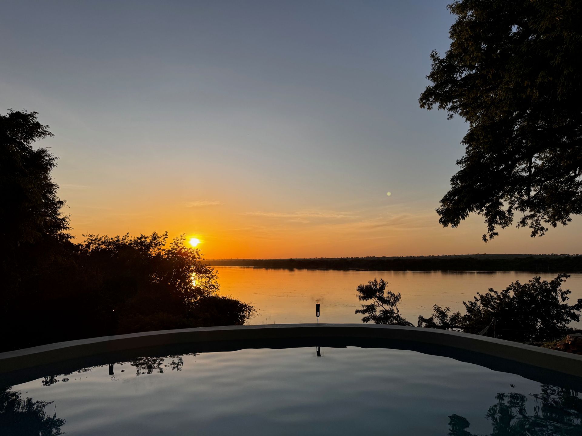Sonnenuntergang über einem Fluss mit ruhigem Wasser und Bäumen am Horizont