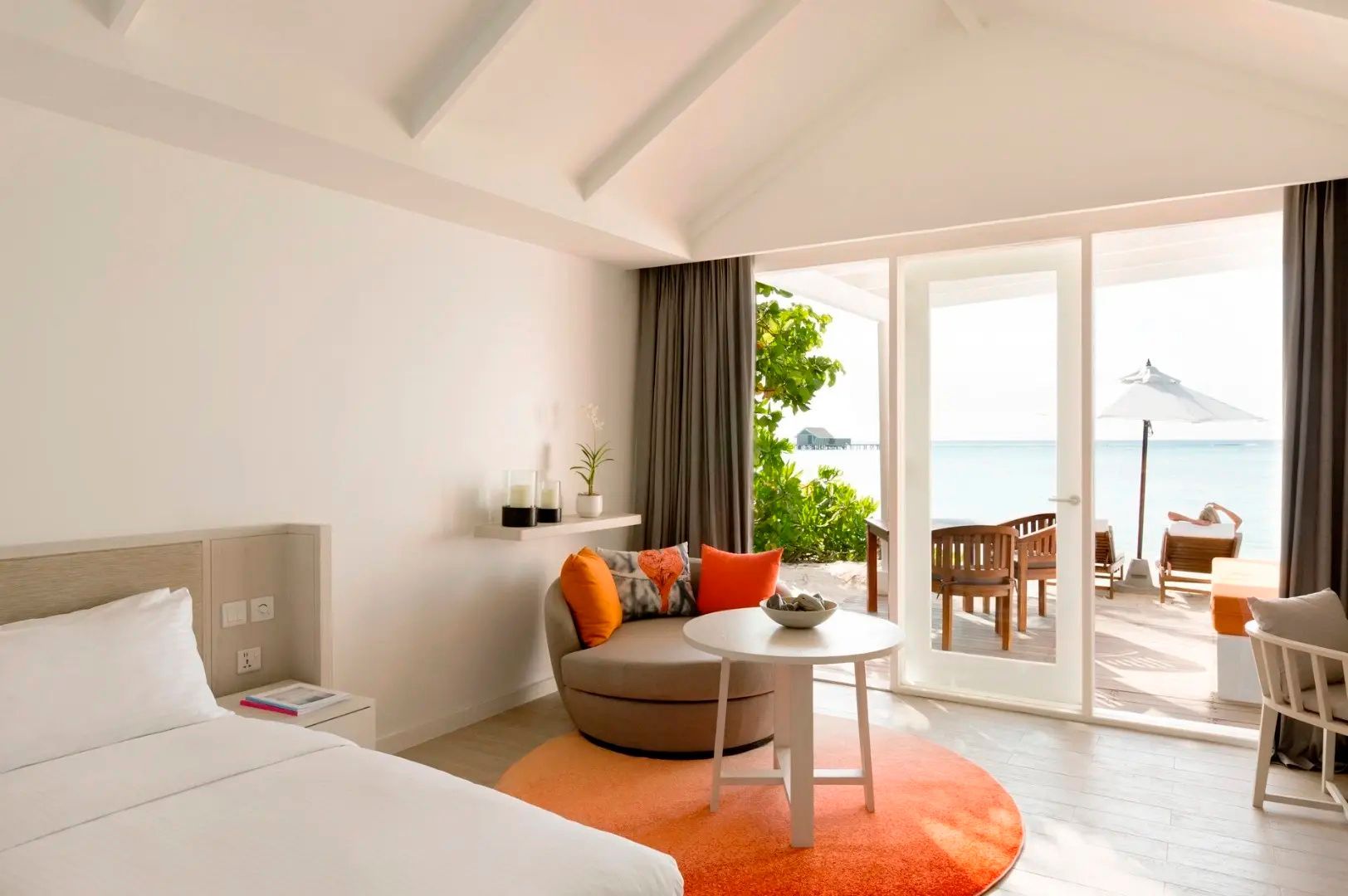 Sitzecke im Hotelzimmer mit runden Möbeln, orangefarbenen Akzenten und Blick auf das Meer.