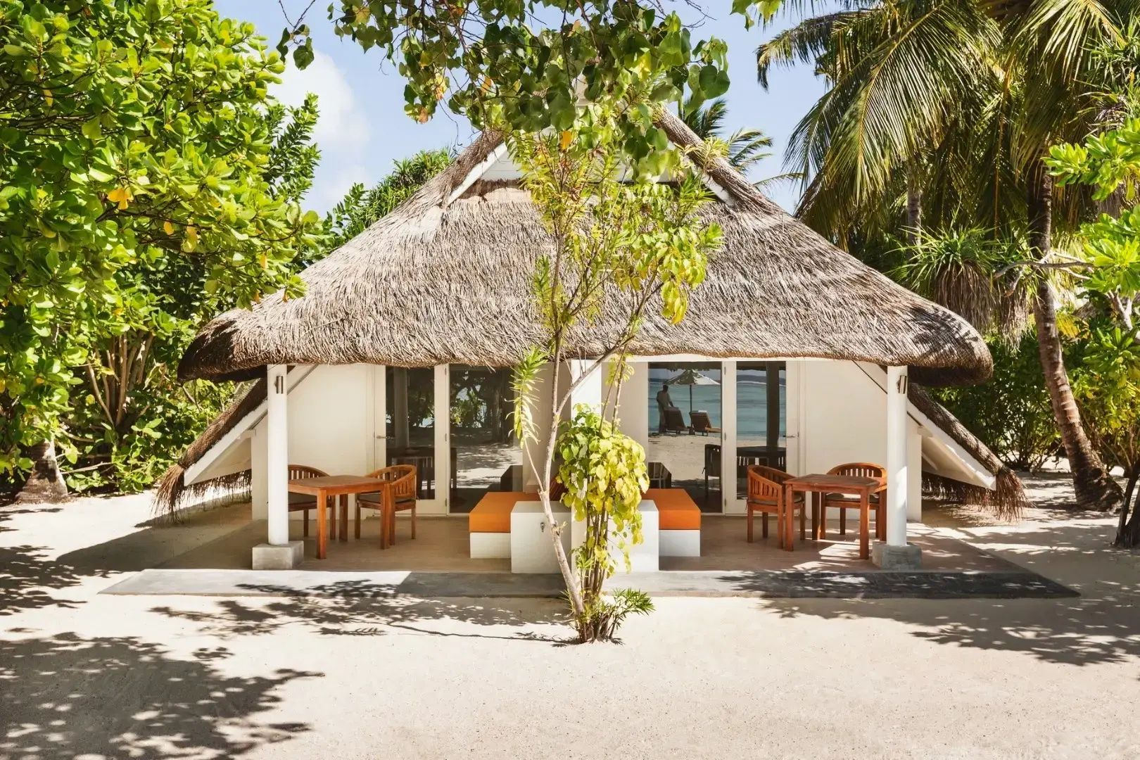 Strandvilla mit Strohdach, überdachter Terrasse und Sitzmöglichkeiten im Sand.