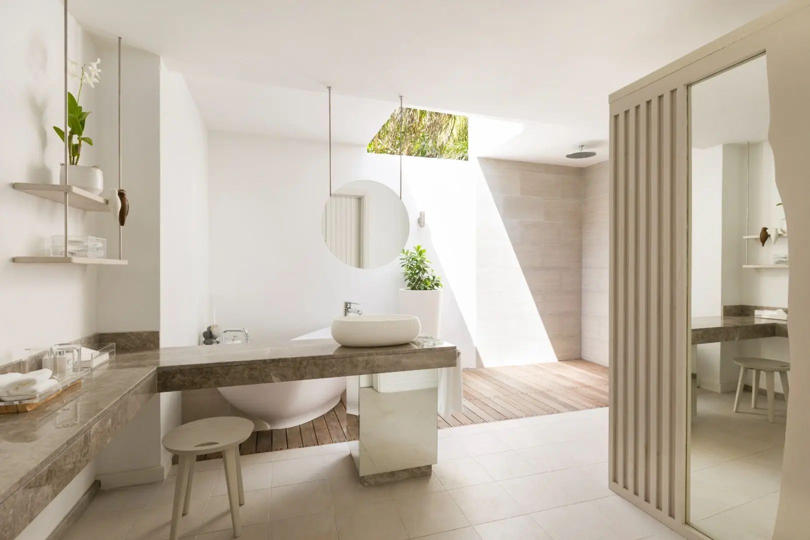 Offenes Badezimmer mit freistehender Badewanne, hellem Fliesenboden und runden Spiegeln.