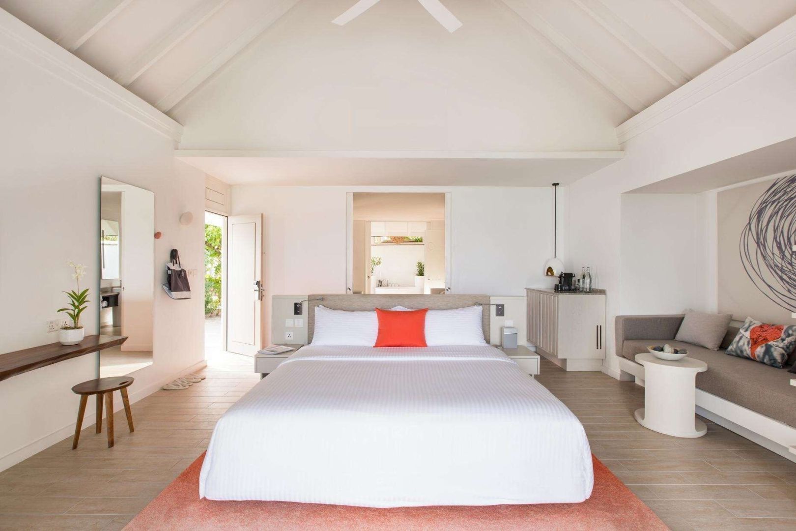 Helles Hotelzimmer mit Doppelbett, orangefarbenem Kissen und hohem Dachfirst.