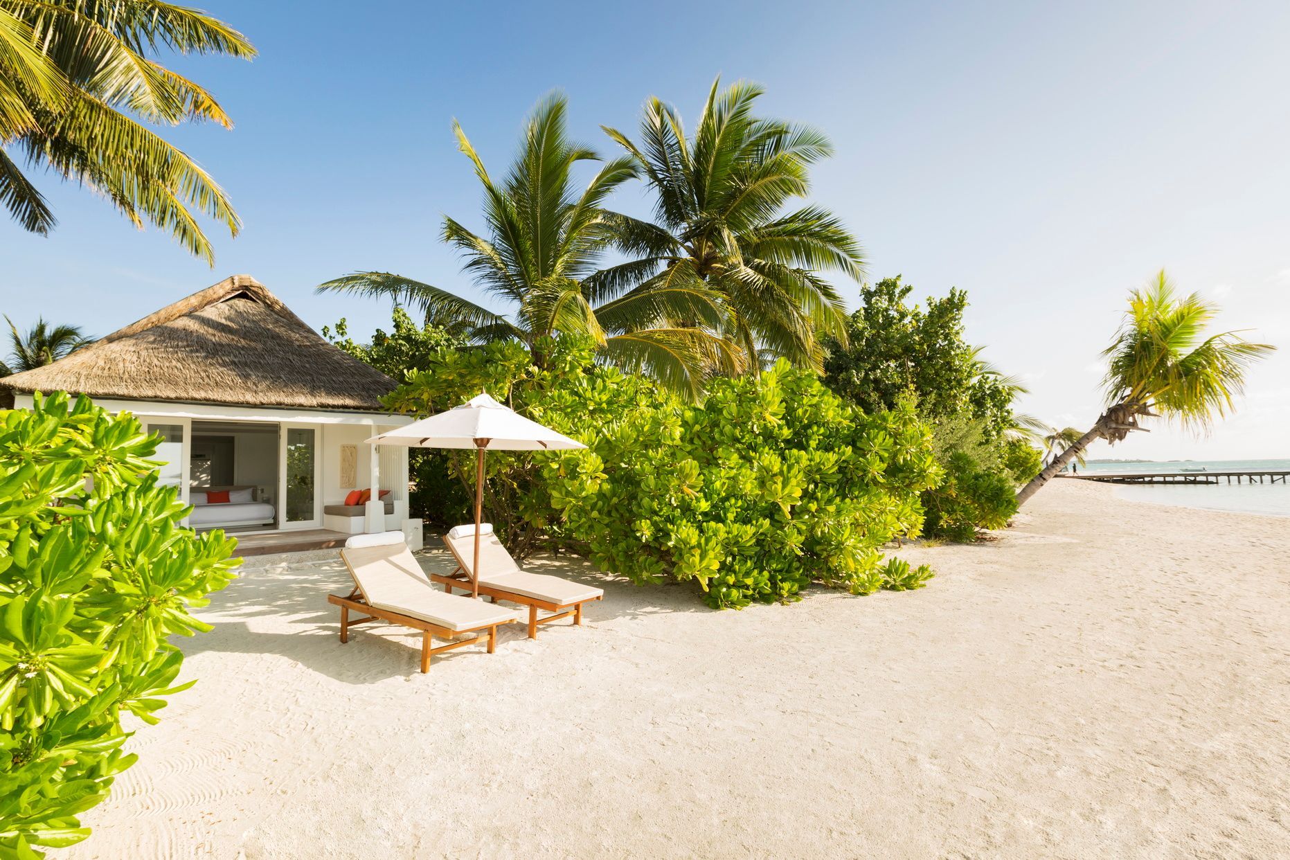 Strandvilla mit Liegestühlen und Sonnenschirm. Umgeben von tropischer Vegetation.