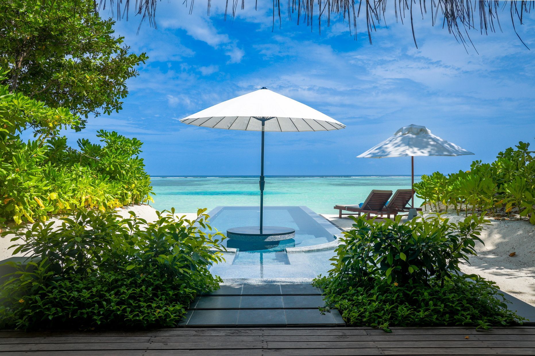 Zwei Liegestühle und ein Sonnenschirm vor einem Pool mit Meerblick