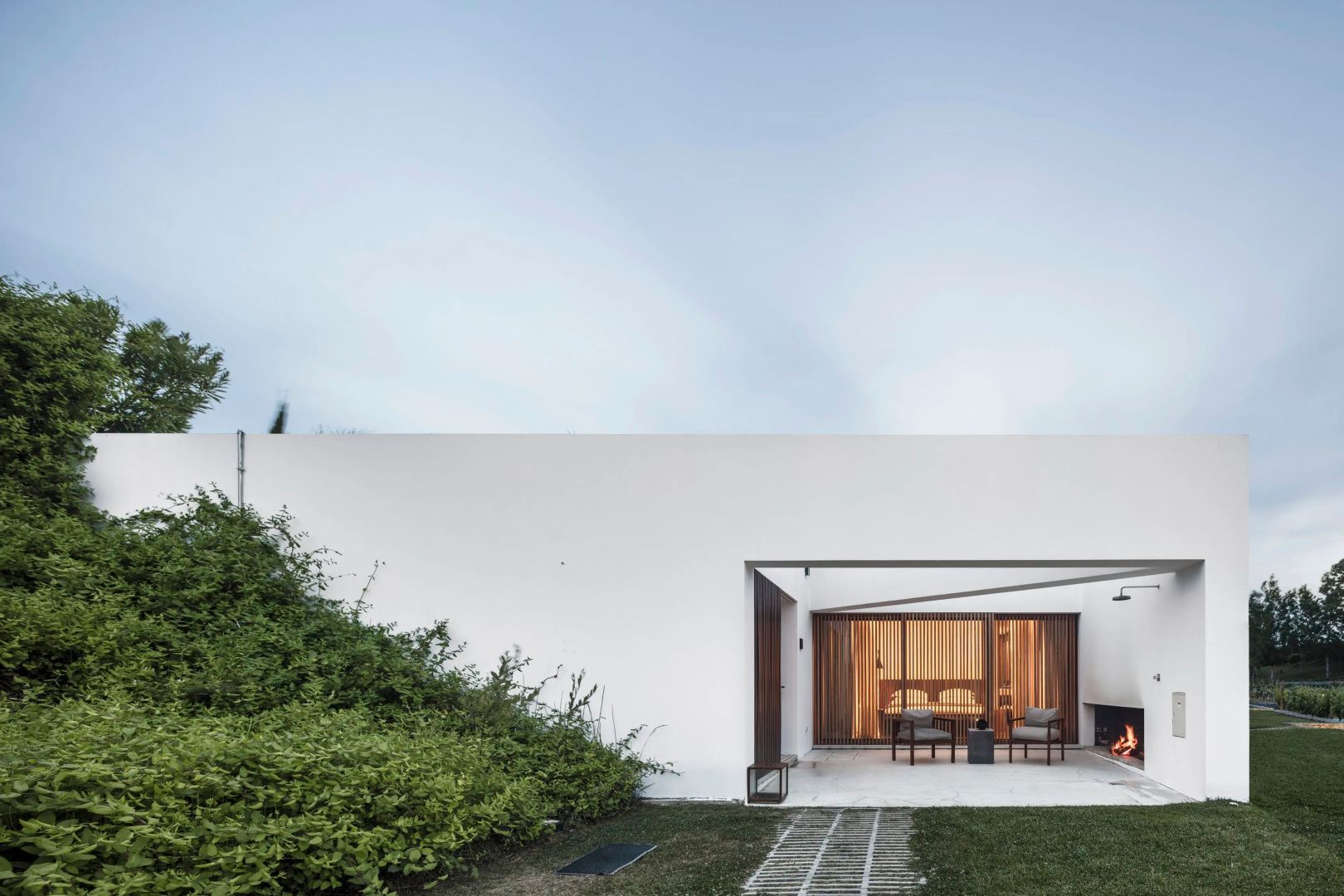 Weiße Gebäudefassade mit begrünter Wand, Rasenfläche und überdachter Terrasse.