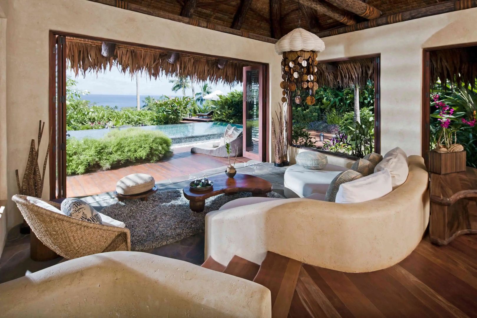 Wohnbereich mit hellem Sofa, Holztisch und Blick auf die Terrasse mit Pool und Meer.