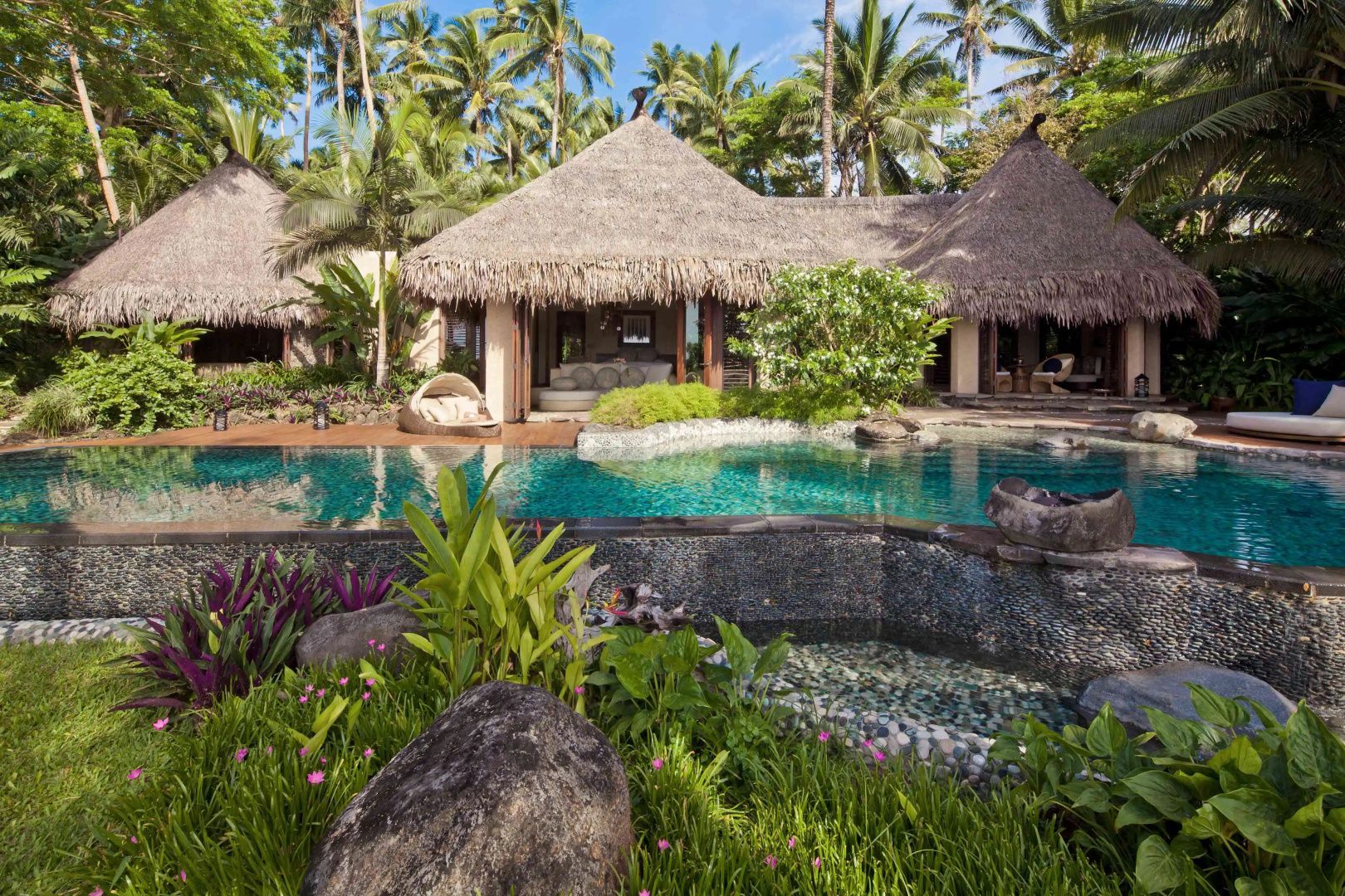Reetgedeckte Villa mit Swimmingpool und tropischen Pflanzen im Außenbereich.