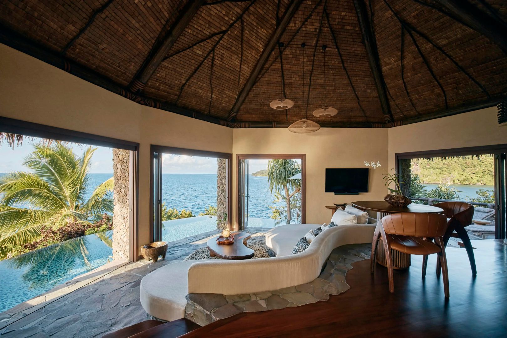 Wohnbereich mit geschwungenem Sofa und großflächigem Blick auf einen Pool und das Meer.