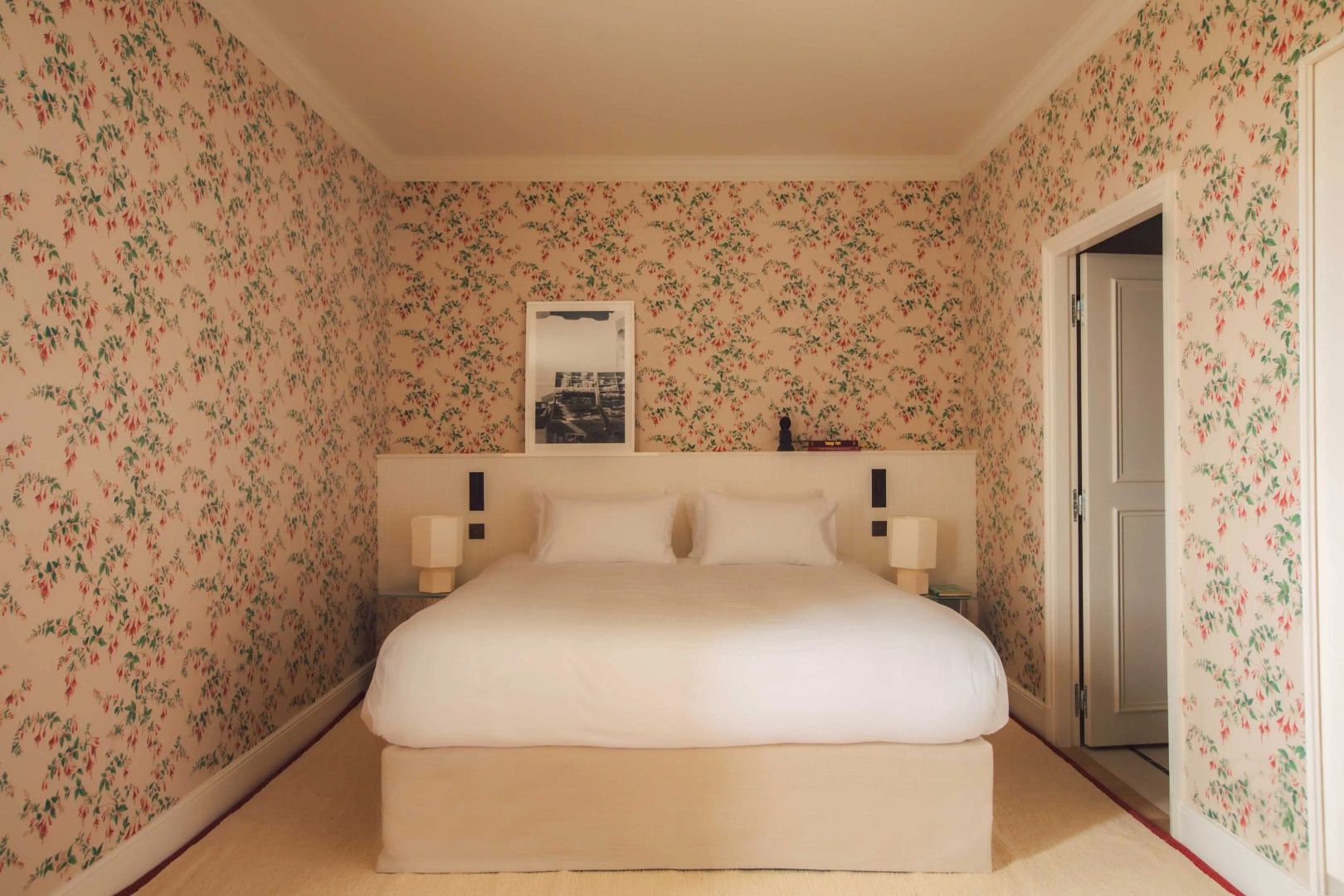 Schlafzimmer mit blumiger Tapete, Doppelbett mit weißer Bettwäsche und Nachttischlampen.