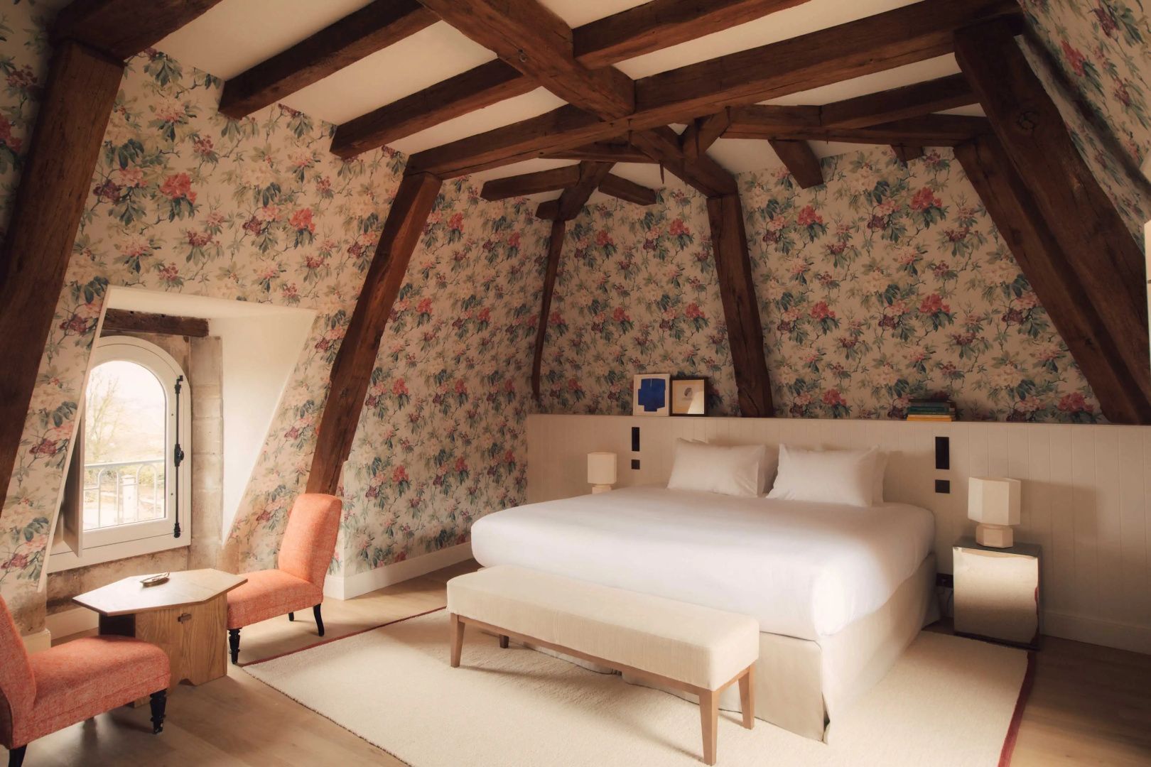 Hotelzimmer im Dachgeschoss mit Holzbalken, Blumenelementen an der Wand und Doppelbett.