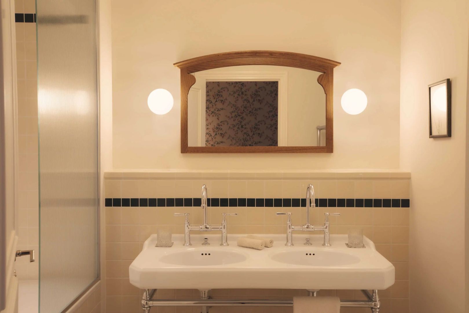 Badezimmer mit zwei Waschbecken, Spiegel im Holzrahmen und runden Wandleuchten.