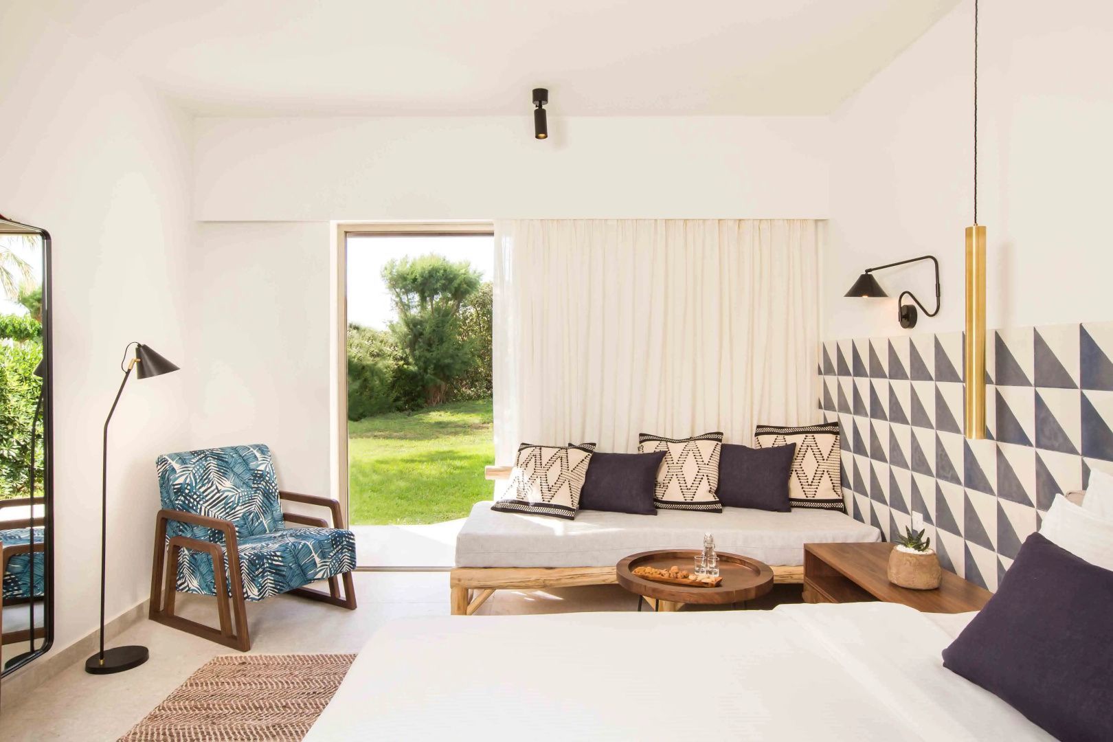 Sitzbereich im Zimmer mit Holzsofa, blauem Sessel und Blick auf den grünen Außenbereich.
