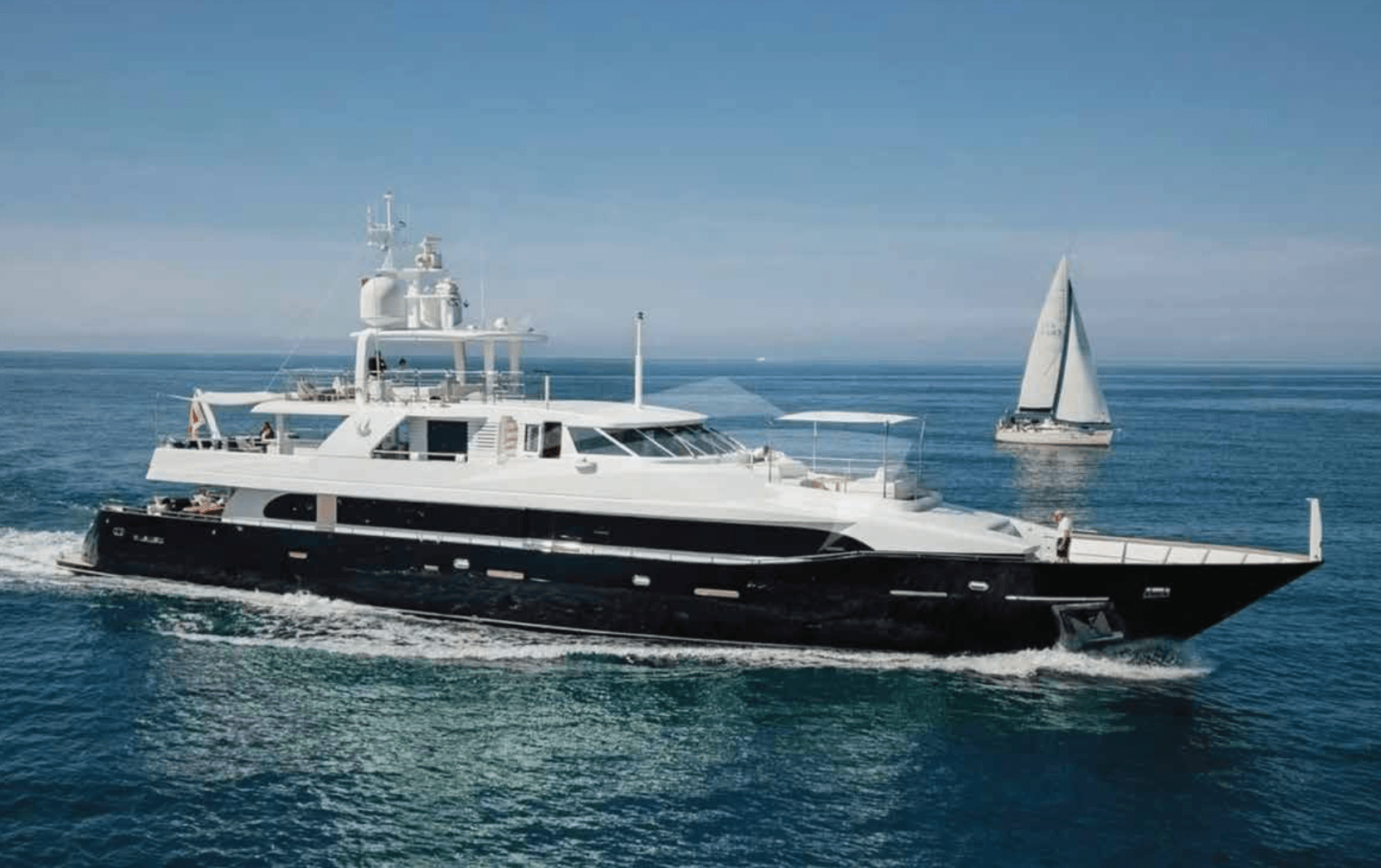 Elegante schwarze Yacht segelt neben kleinem Segelboot auf ruhigem Wasser