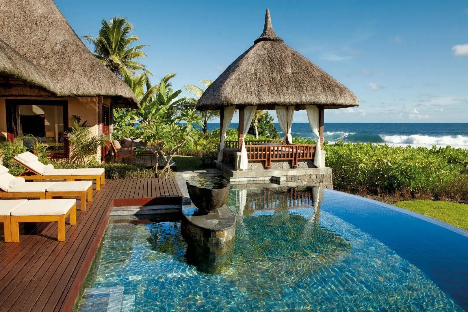 Privater Pool mit Holzdeck, strohgedecktem Pavillon und direktem Blick auf den Ozean.