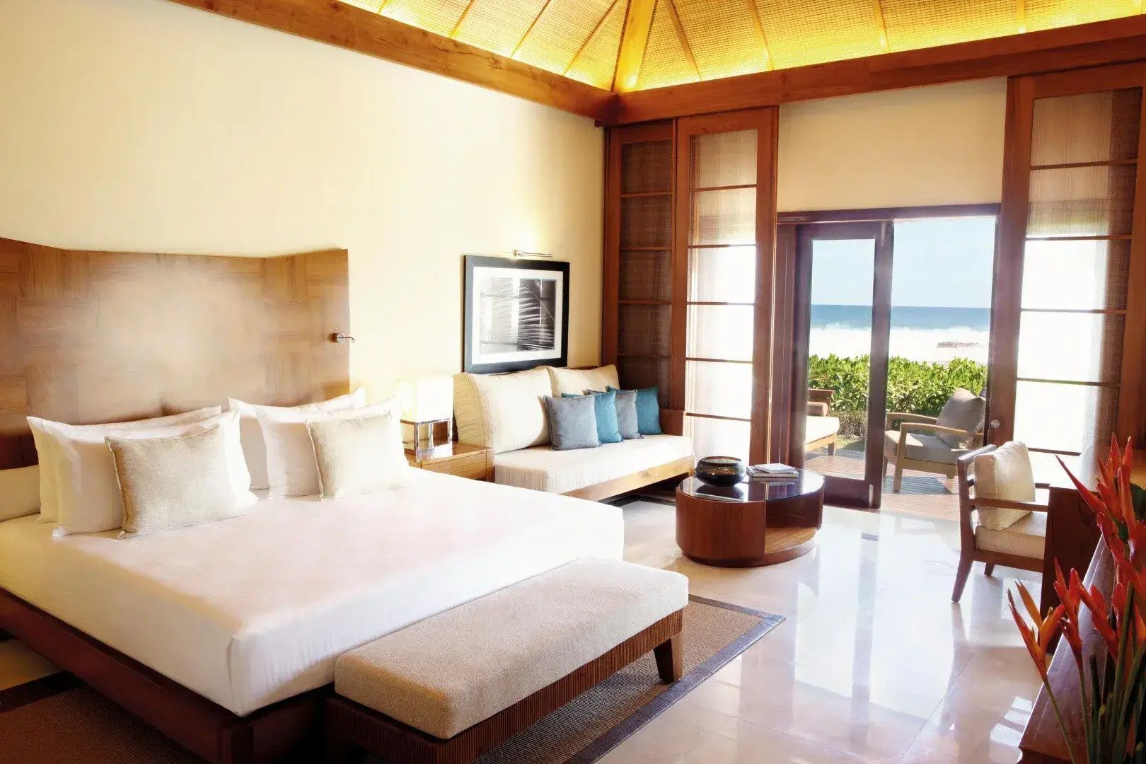 Helles Schlafzimmer einer Villa mit Doppelbett, Sitzbereich und Blick auf das Meer durch die Terrassentür.