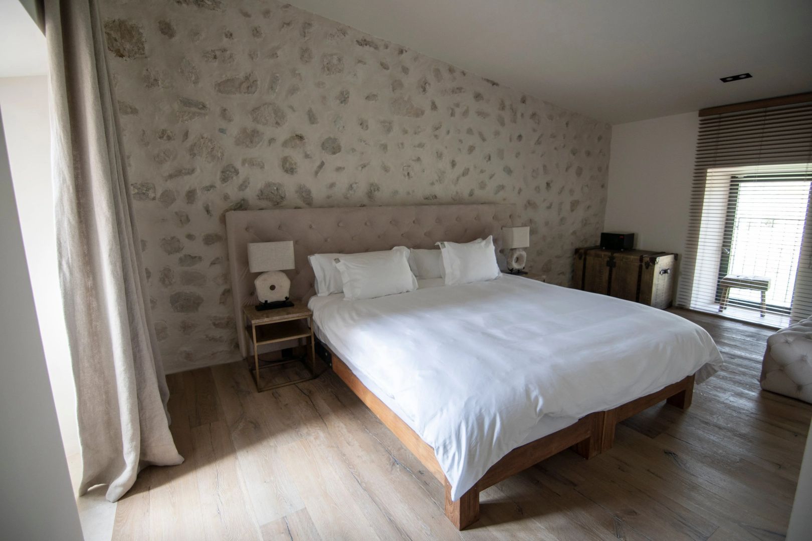 Doppelbett mit weißer Bettwäsche vor einer rustikalen Steinwand im Schlafzimmer.