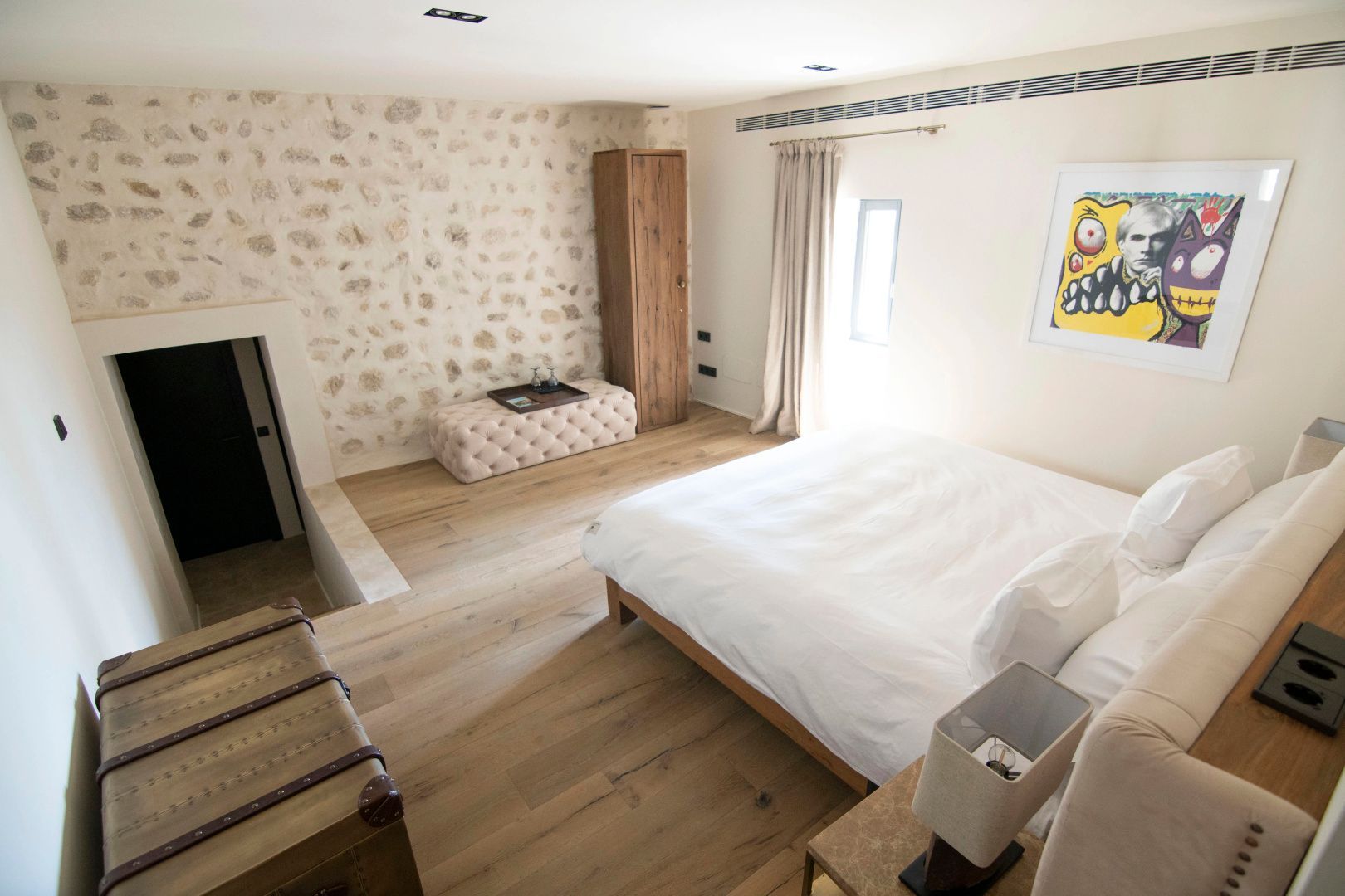 Helles Schlafzimmer mit Holzfußboden, großem Doppelbett und Natursteinwand.