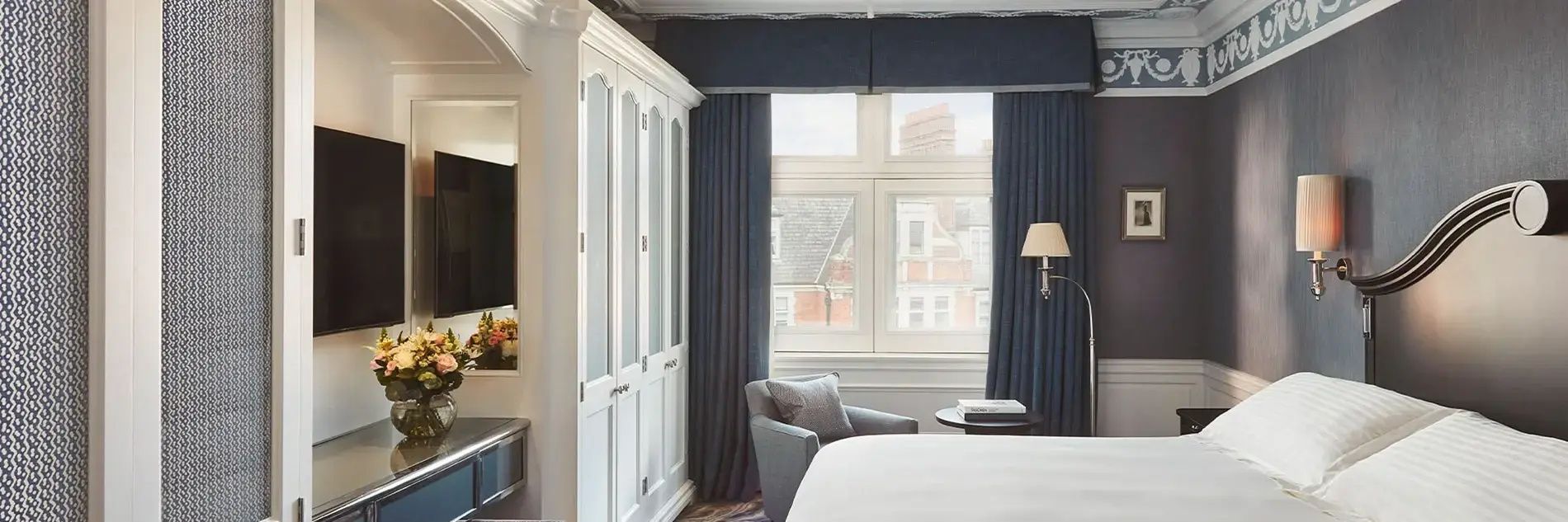 Weißer Kleiderschrank und blauer Sessel an einem Fenster mit Vorhängen.