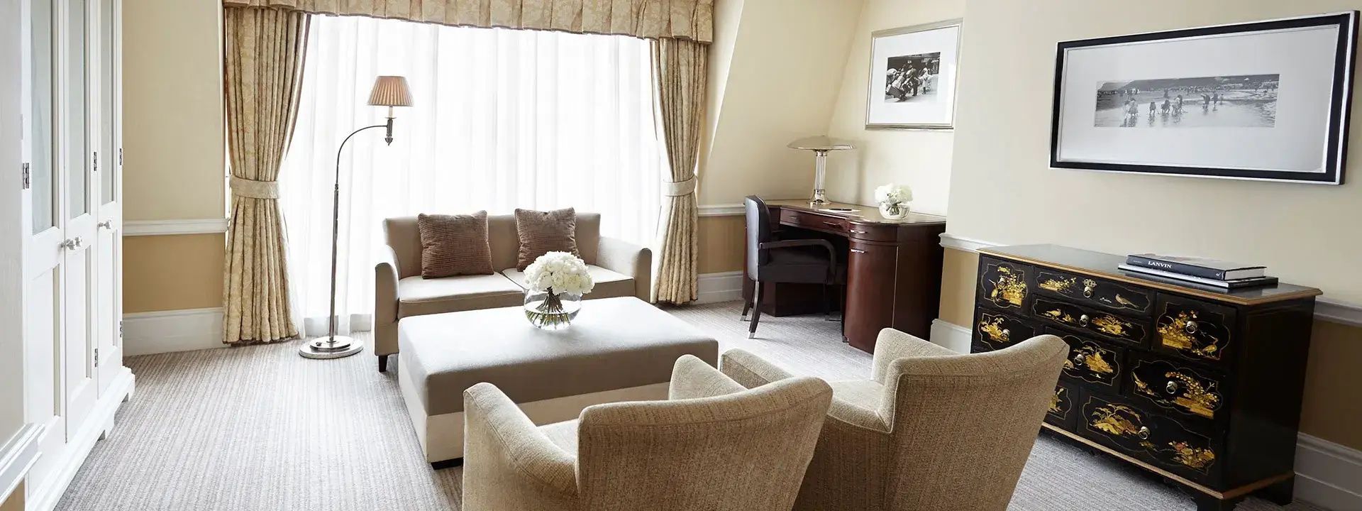 Wohnbereich eines Hotelzimmers mit beigefarbenem Sofa, Sesseln und einem dunklen Schreibtisch.