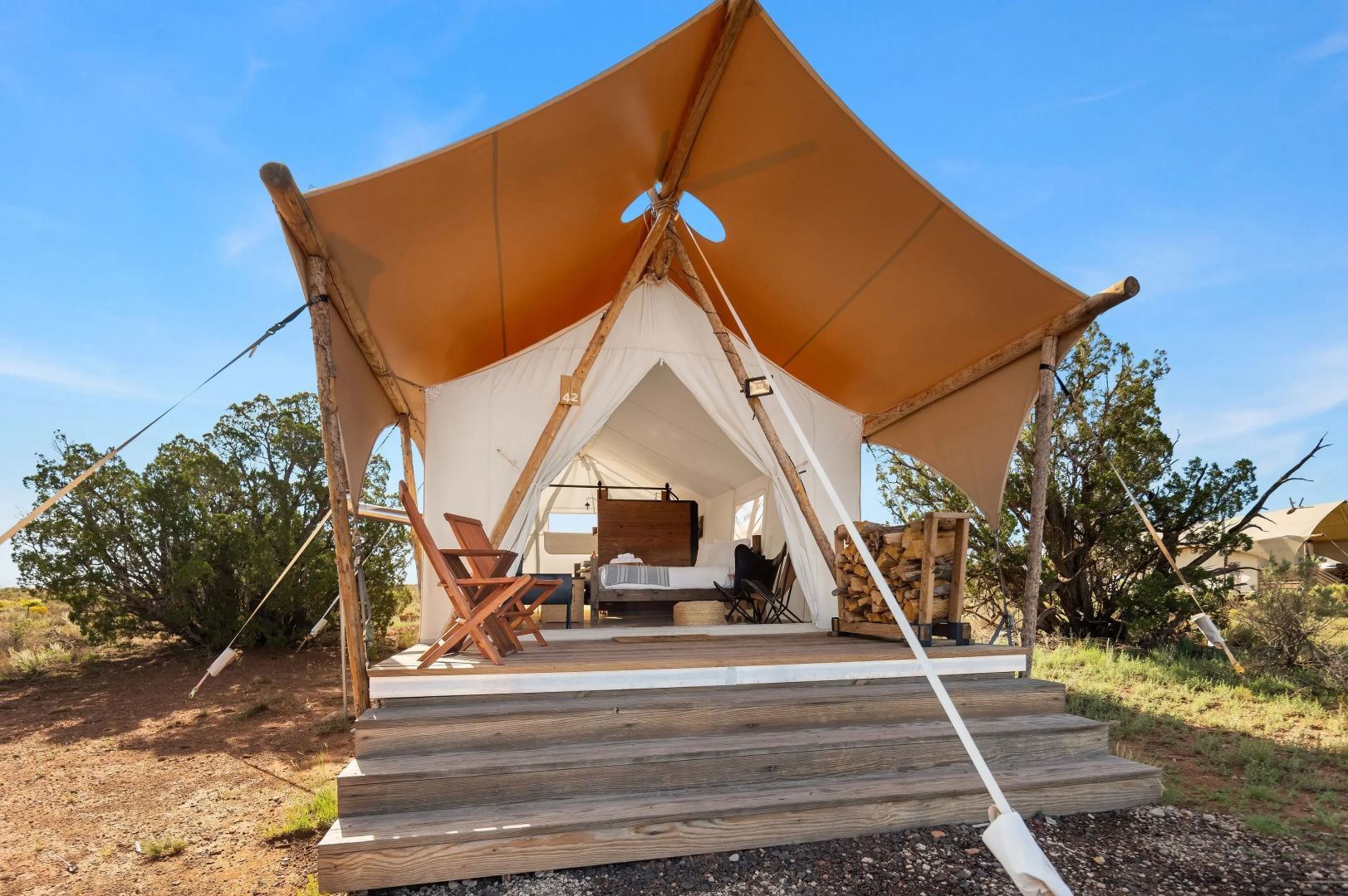 Glampingzelt auf einer Holzplattform mit Stühlen und Blick auf das Bett im Inneren.