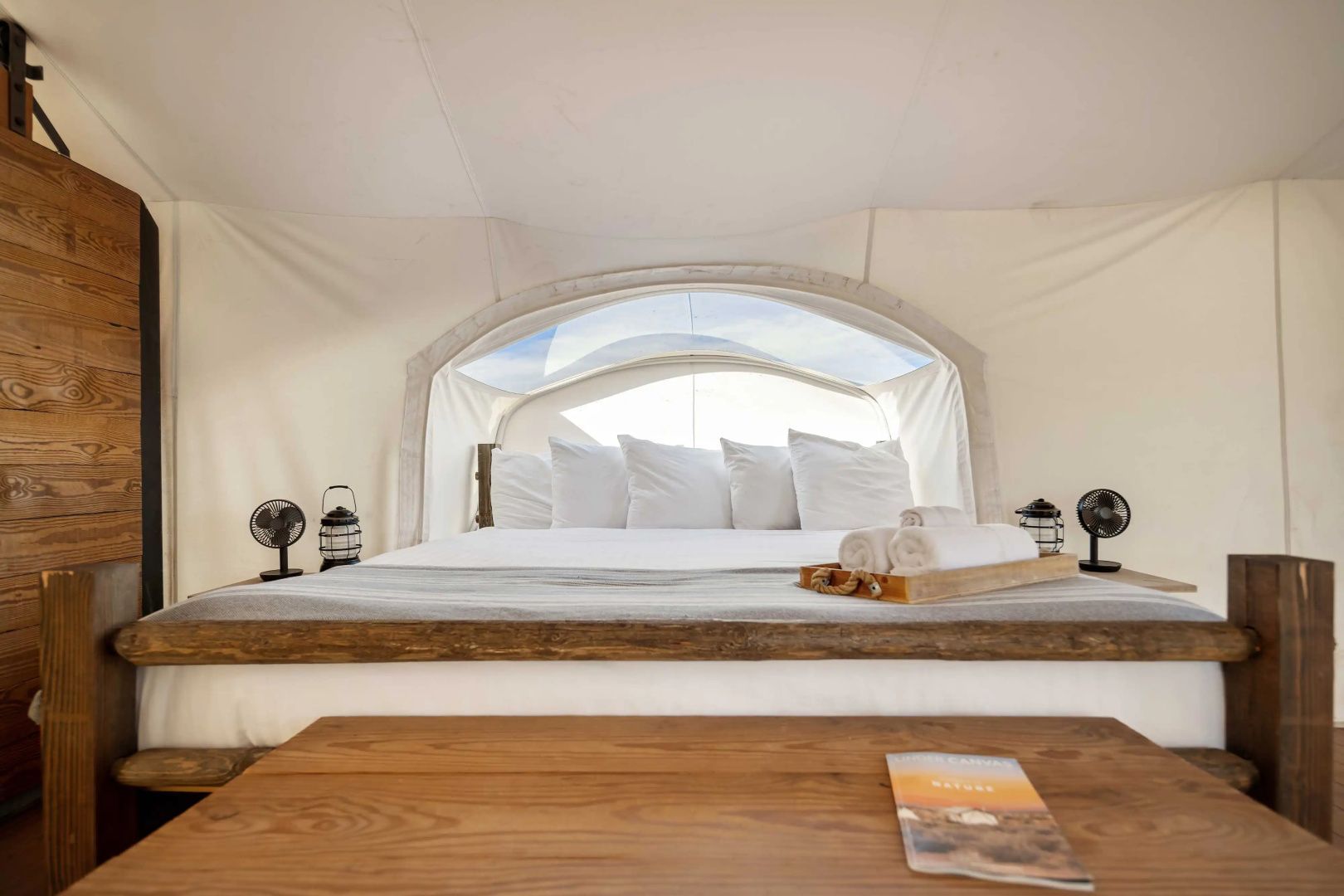 Doppelbett mit Kissen und Blick durch ein Sichtfenster in der Zeltwand.