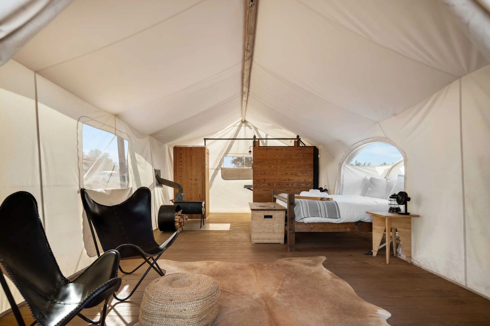 Einrichtung im Zelt mit Ledersesseln, Fellteppich, Holzofen und Bett.