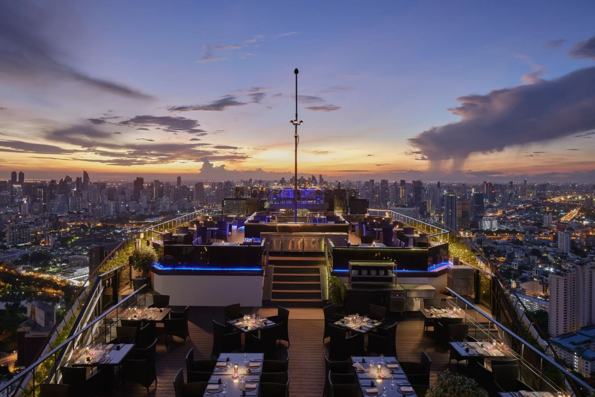 Rooftop-Bar bei Sonnenuntergang mit Blick auf die Skyline einer Metropole.