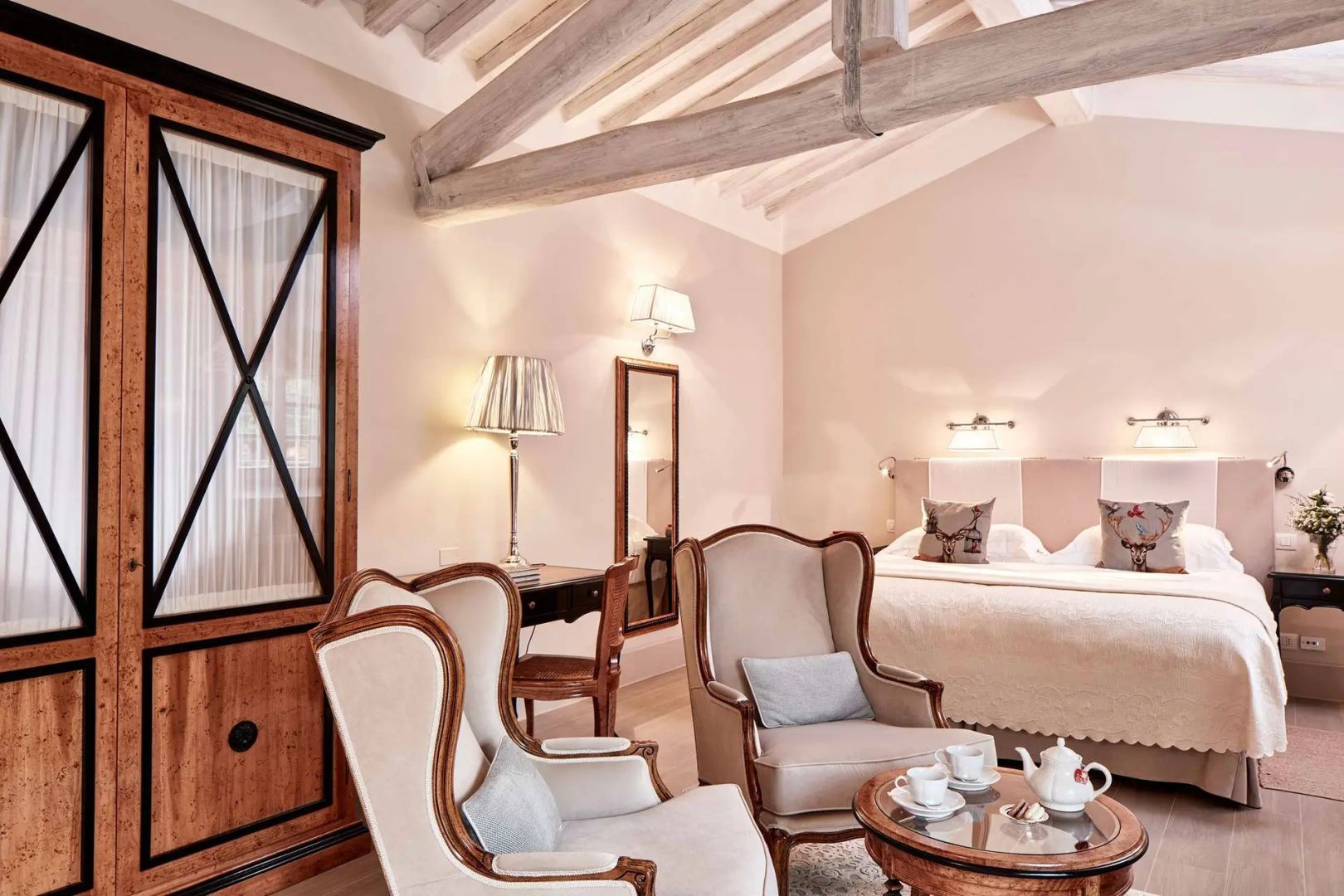 Hotelzimmer mit sichtbaren Holzbalken, zwei Sesseln und einem Doppelbett im Hintergrund.