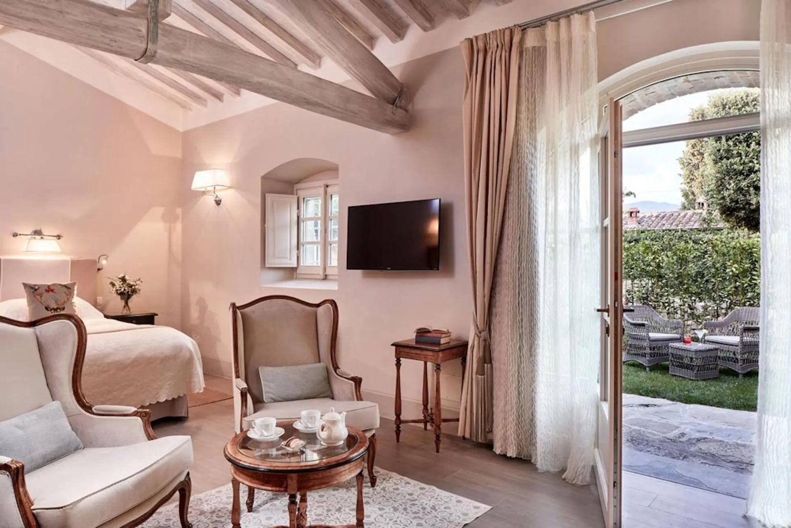 Wohnbereich eines Hotelzimmers mit Fernseher, Sesseln und Zugang zur Terrasse.