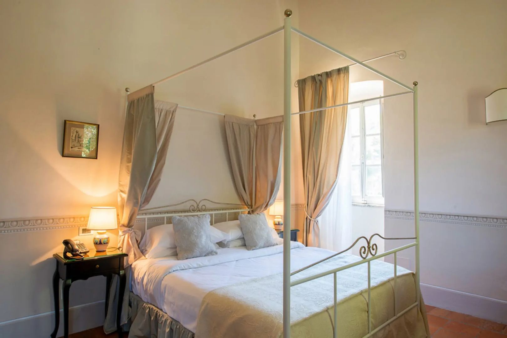Himmelsbett aus weißem Metall mit hellen Vorhängen und beigen Kissen im Schlafzimmer.