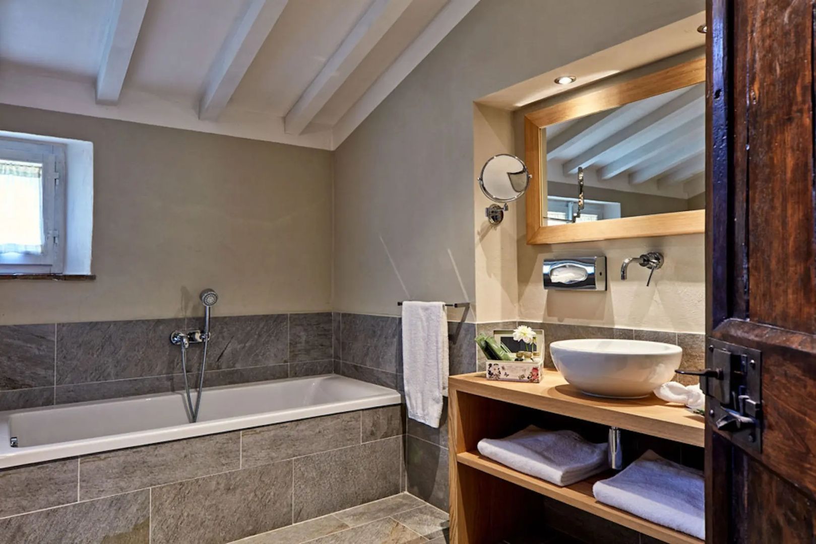Badezimmer mit grau gefliester Badewanne und Waschtisch aus Holz mit Aufsatzwaschbecken.