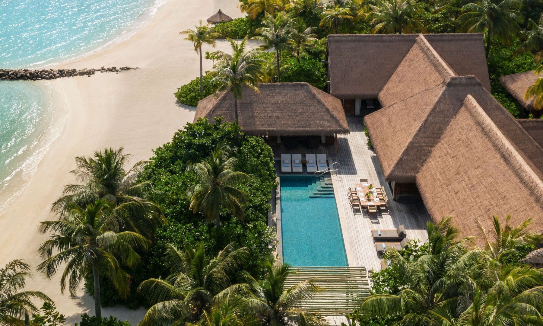 Luftaufnahme einer Strandvilla mit privatem Pool, Holzdeck, Palmen und Sandstrand.