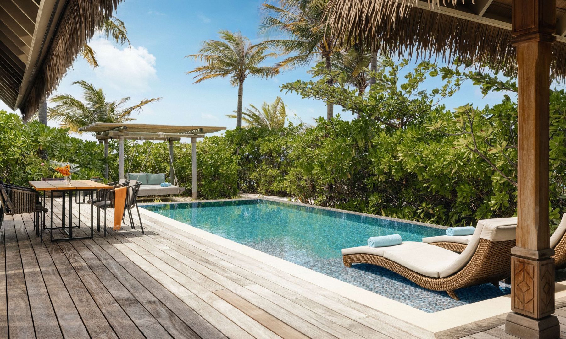 Privater Außenpool mit Holzterrasse, Sonnenliegen und tropischer Bepflanzung.