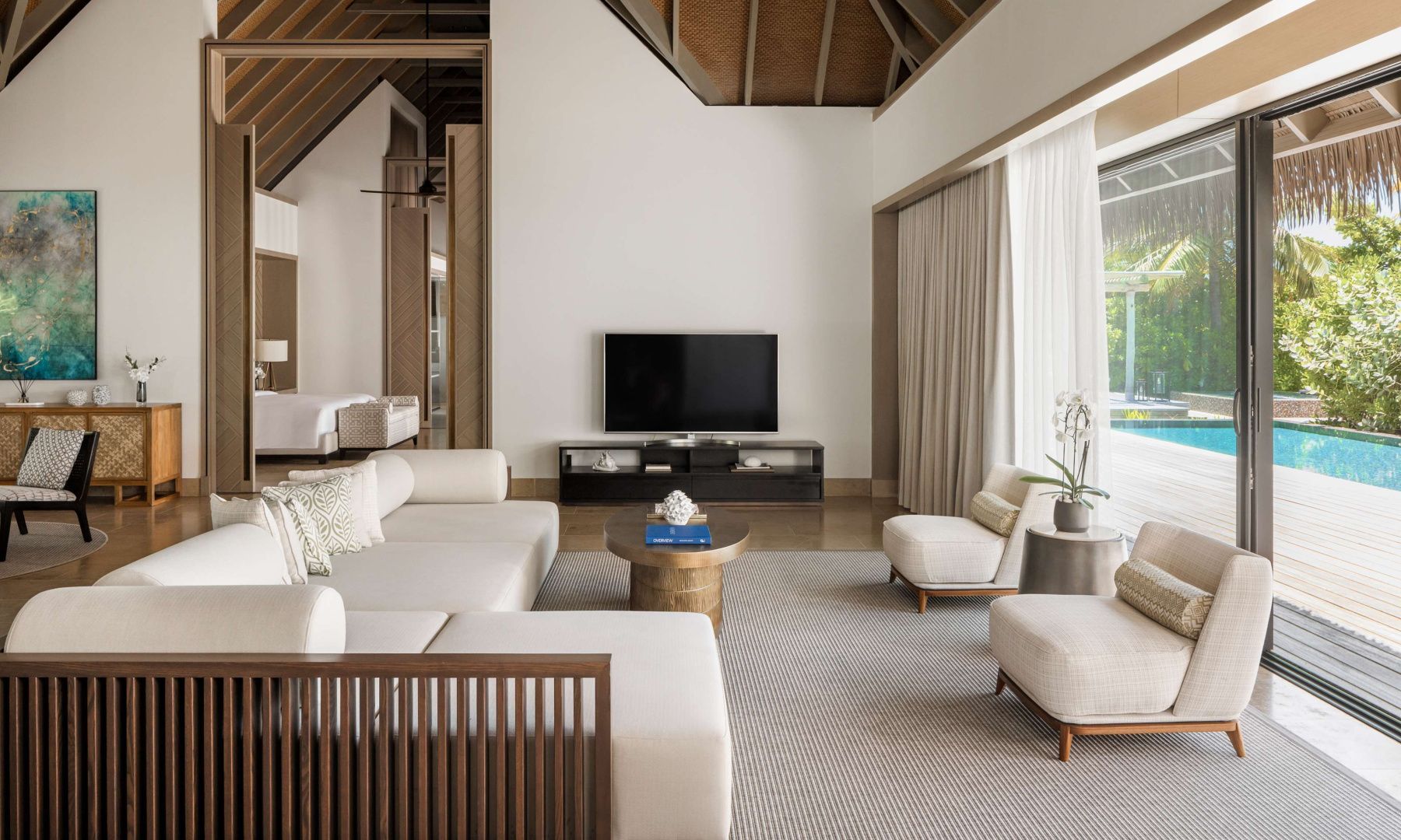 Heller Wohnbereich einer Villa mit beigen Sofas, Fernseher und hoher Holzdecke.