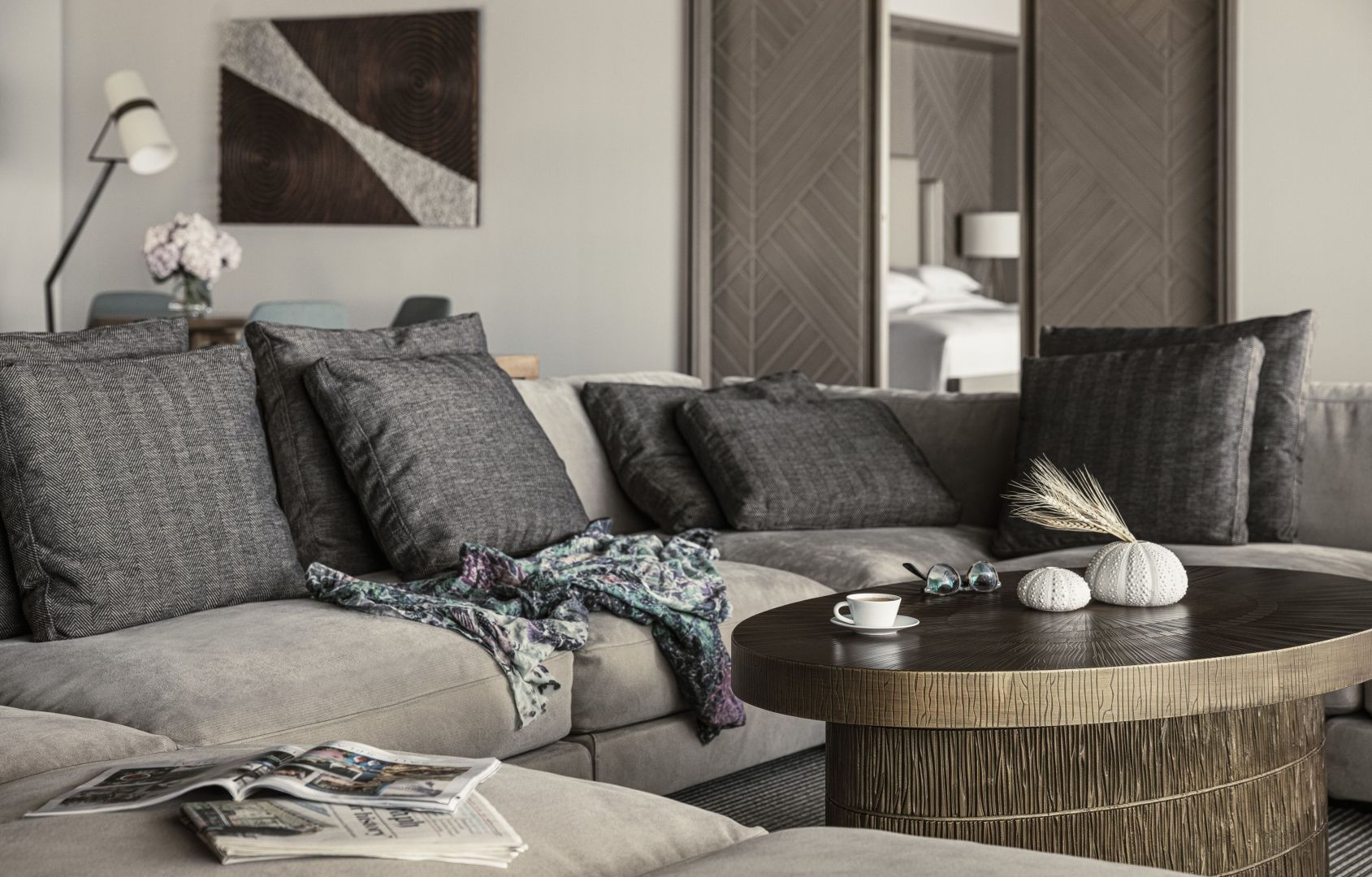 Sitzbereich mit grauem Ecksofa, Kissen und einem dunklen Holztisch im Wohnraum der Suite.