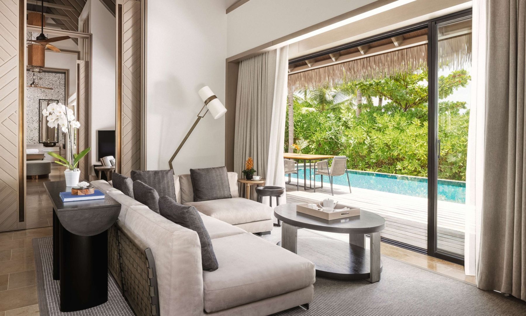 Wohnbereich einer Villa mit hellem Sofa, Couchtisch und Blick auf die Terrasse mit Pool.