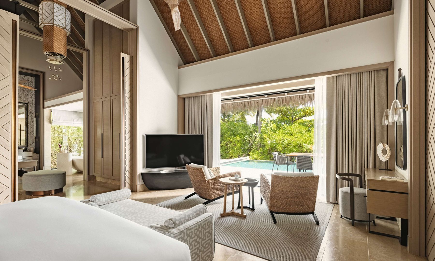 Zimmer mit Fernseher, Sesseln und großer Glasfront zur Terrasse mit privatem Pool.