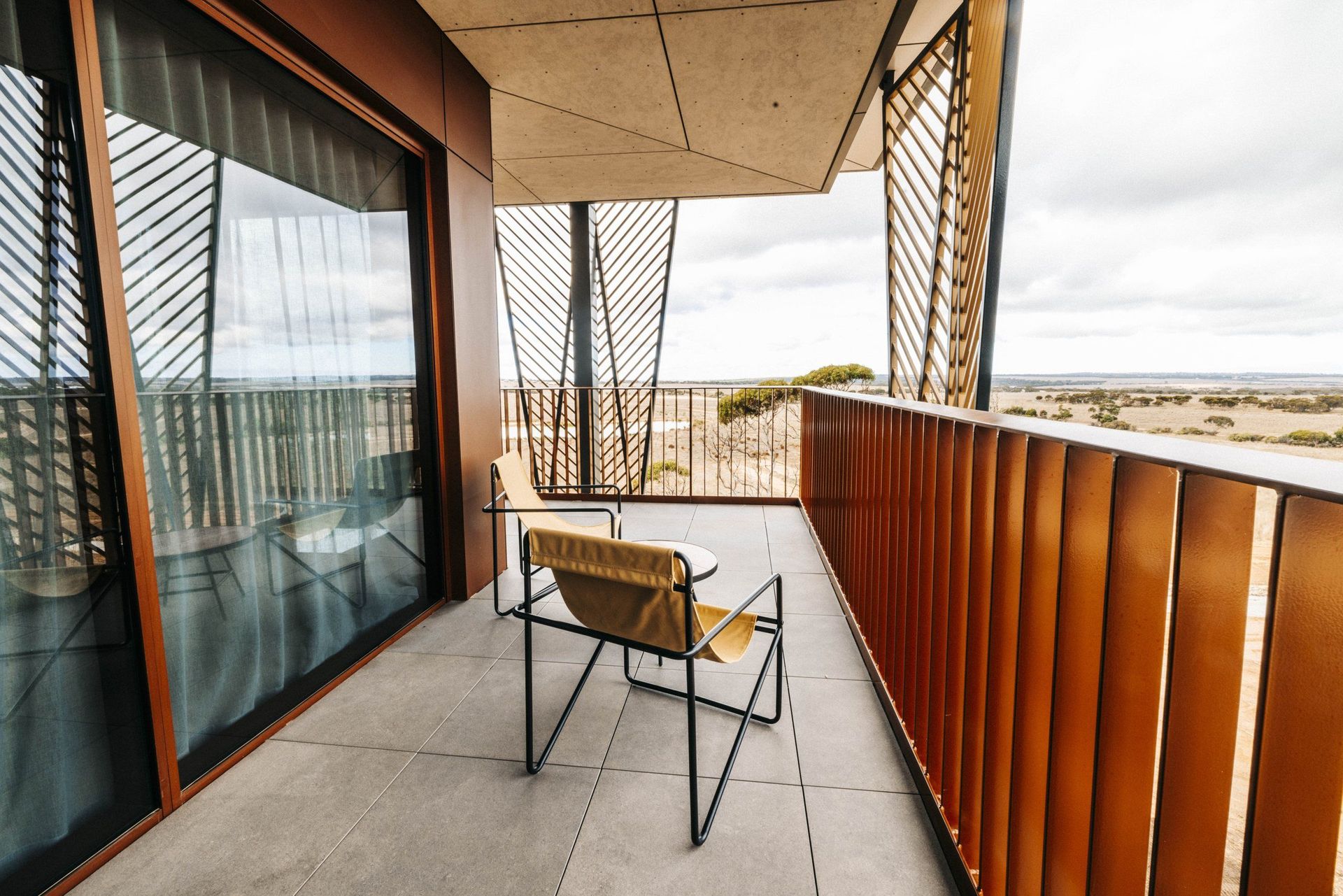 Balkon eines Resortzimmers mit zwei Stühlen, Holzverkleidung und Blick über die Savanne