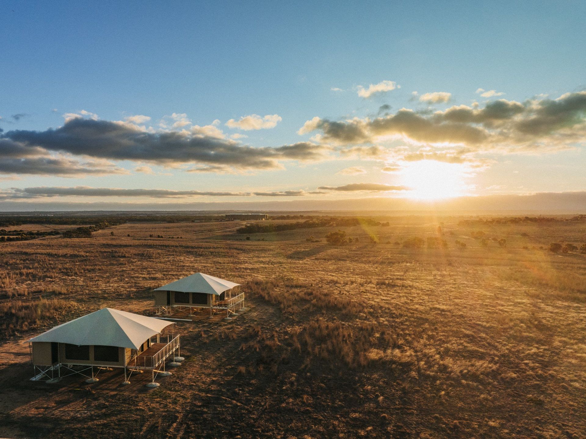 Zwei Safari-Lodge-Zelte auf Stelzen in der Savanne bei Sonnenuntergang von oben