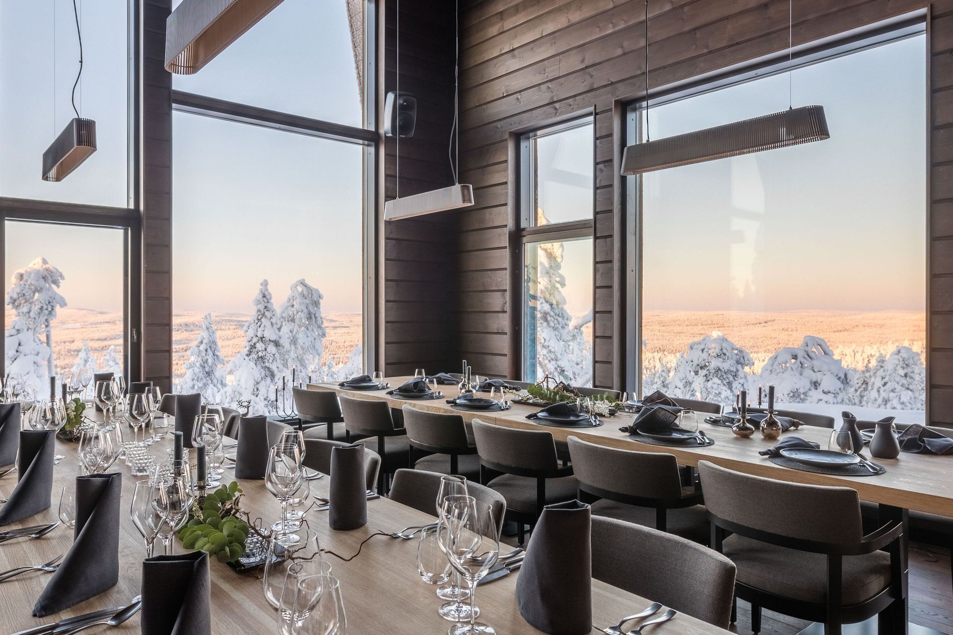 Lange gedeckte Tafel in der Octola Lodge vor Panoramafenstern mit Blick auf verschneite Bäume