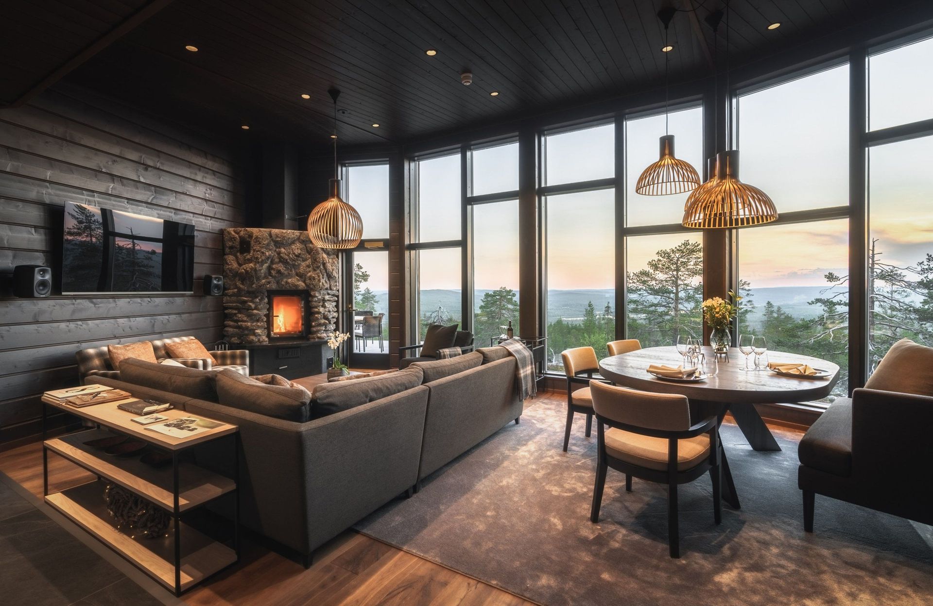 Wohnraum der Octola Villa mit Kamin, Sofa und Esstisch vor Fenstern zur Sommerlandschaft
