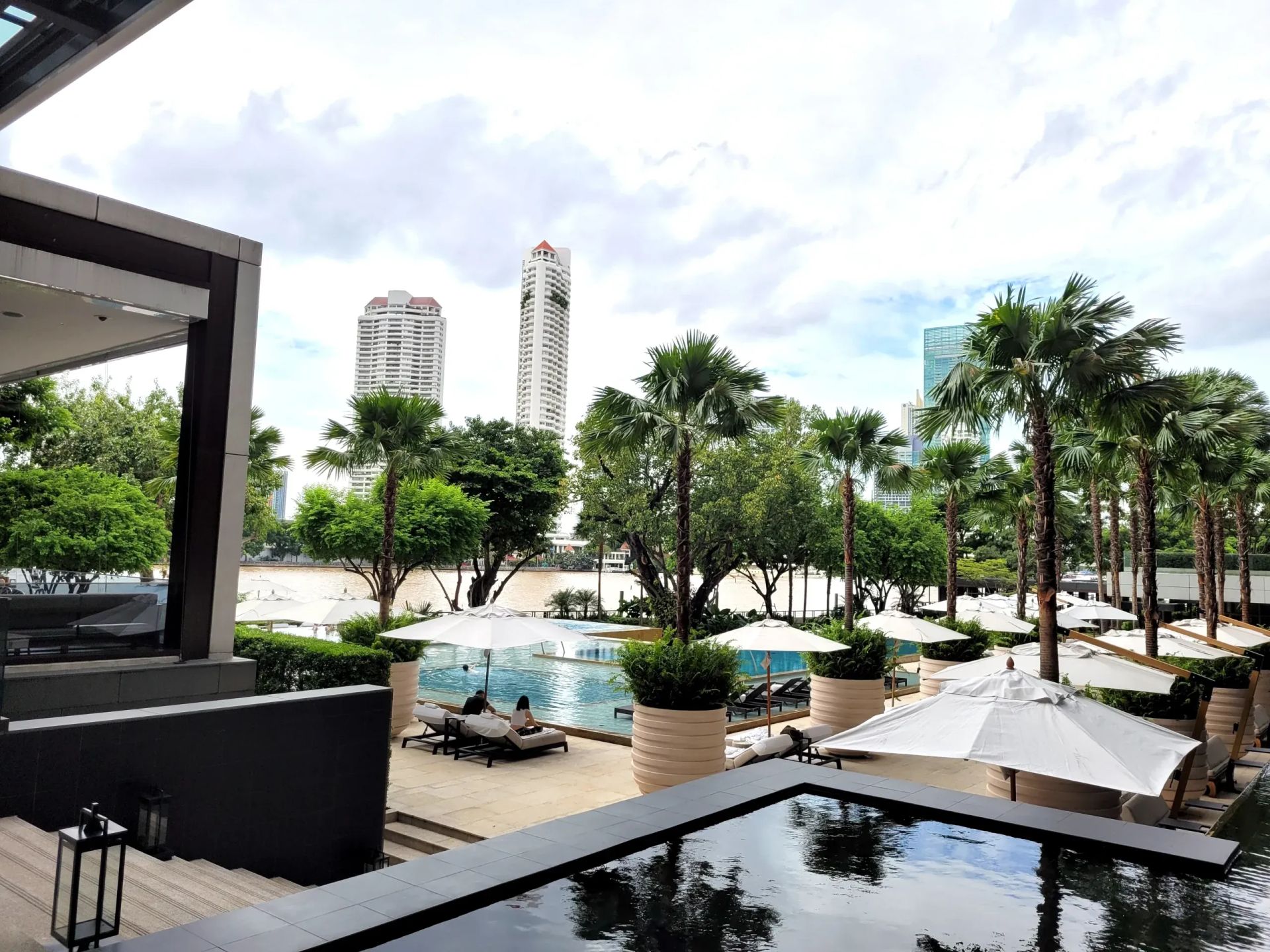 Four Seasons Bangkok Außenbereich mit Pool, Palmen und Blick auf Skyline Gebäude